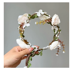 Detailed close-up of white satin flowers and green leaves on a vine floral headband