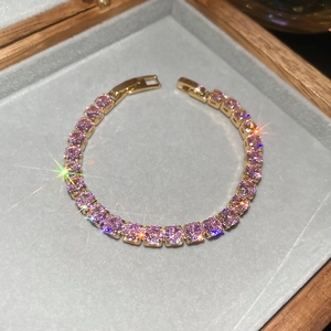 Macro detail of a gold link bracelet with pink cubic zirconia in a velvet box