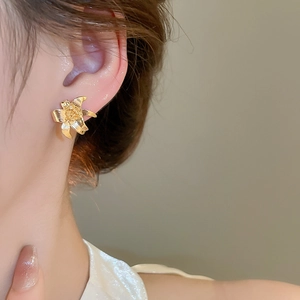 Detailed close-up of golden lily flower earring showing metallic texture and petals