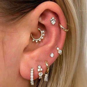 Detail of gold S925 silver cartilage piercings with cubic zirconia on ear lobe and helix