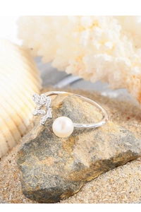 Macro detail of silver flower and pearl ring on a beach rock with seashell background