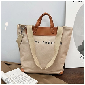 Detail of beige canvas tote bag with brown leather handles and black fashion lettering