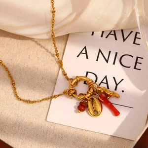 Detail of gold shell and red bar pendants on a beaded chain necklace in sunlight