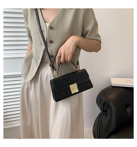 Detail of black leather crossbody bag with gold buckle lock and detachable strap on a model