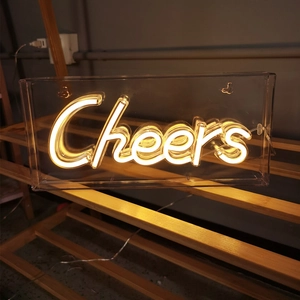 Cheers neon sign with warm yellow LED glow in acrylic box on a wooden shelf