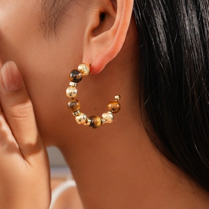 Detail view of 16K gold-plated C-shaped earrings with amber tiger eye beads on model