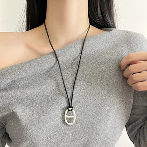Minimalist silver flower pendant necklace with black cord worn by a model on a grey top