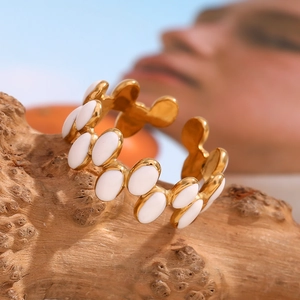 Close-up of gold-plated stainless steel ring with white enamel ovals on wood