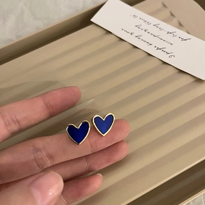 Detail of gold-edged heart earrings with deep blue enamel inlay held over a tray