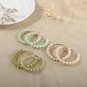 Detail view of handmade gold wire hoop earrings with colorful pearl beads on beige fabric