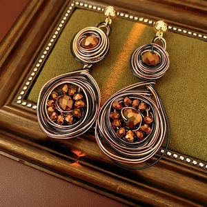 Detail view of vintage woven round earrings with gold beads on green velvet inside wood frame