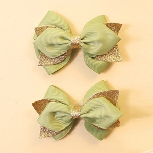 Detailed close-up of green and gold glitter bow hair clips for kids on beige background