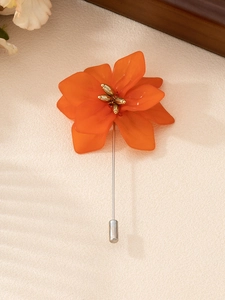 Macro detail of elegant orange flower brooch with delicate resin petals and silver pin