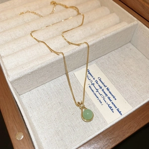 Detailansicht einer goldenen Halskette mit grünem Jadestein in einer hochwertigen Holzbox
