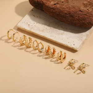 6 pairs of gold-plated geometric hoop earrings set with rhinestones on stone background