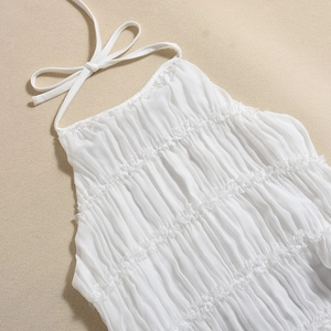 Close-up of white halter dress featuring delicate layered ruffles and pleated fabric