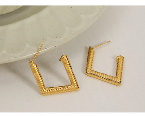 Macro detail of square gold earrings with twisted rope texture on a white wooden background