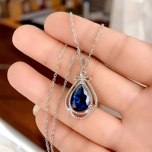 Macro shot of blue pear-shaped sapphire pendant with bow detail and silver chain