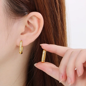 Detailed view of U-shaped gold geometric earrings with white zircon on a model