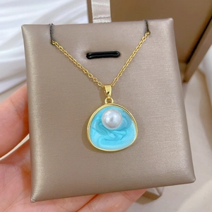 Vue macro d'un collier en titane doré avec perle blanche et pendentif en émail bleu