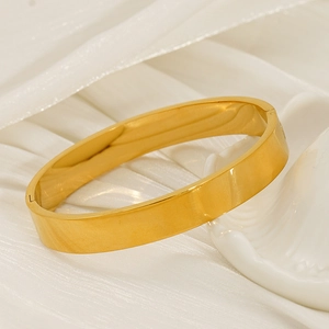 Polished 18K gold minimalist bangle with snap closure on elegant white silk background