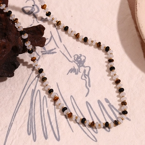 Detail of beaded necklace featuring white, brown tiger eye, black beads and gold spacers