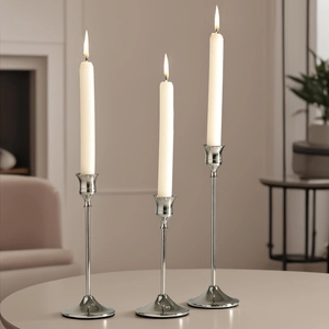 Modern set of three silver polished metal candle holders with lit white taper candles
