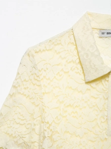Detail of pale yellow lace shirt showing delicate floral patterns and polo collar