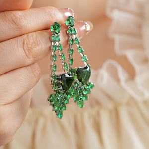 Detailed close-up of heart-shaped green gemstone earrings with silver-tone leaf accents