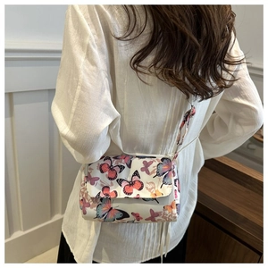 Detail of a white square shoulder bag featuring vibrant butterfly prints on a model