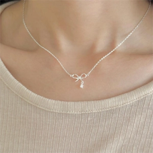 Close-up of a silver bow necklace with a zircon pendant on a model wearing beige knitwear