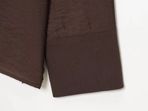 Detailed close-up of dark brown long-sleeved shirt cuff and textured pleated fabric