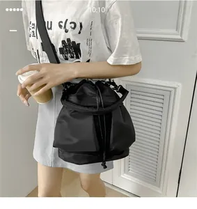 Detail of black nylon drawstring bucket bag with wide strap worn by a model