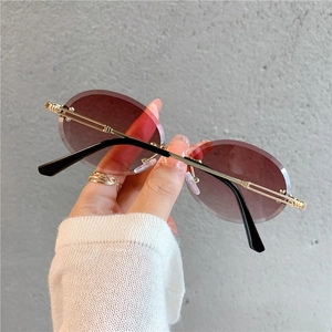 Détail de lunettes de soleil ovales sans monture, verres dégradés violets et branches d'or