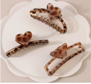 Detail of leopard print hair claw clips with heart charm on a white cloud tray