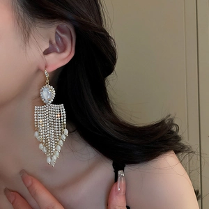 Close-up of sparkling rhinestone tassel earrings with white pearls on a side-view model