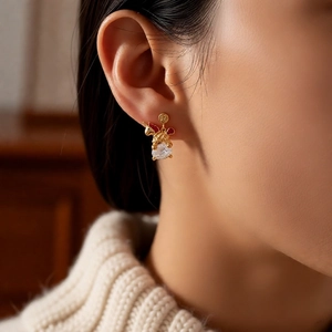 Close-up of golden unicorn earrings with red enamel and pear-cut zircon on model's ear