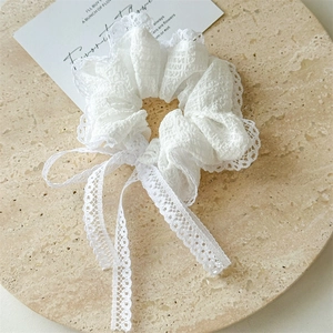 Detailed close-up of a white lace scrunchie with long tassel ribbons and floral embroidery