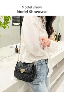 Detail of a black quilted crossbody bag with heart buckle worn on a white shirt