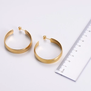 Macro detail of gold hoop earrings showing textured diagonal stripes and size measurement