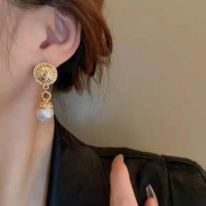 Close-up of vintage gold embossed earrings with white pearl pendant worn by model