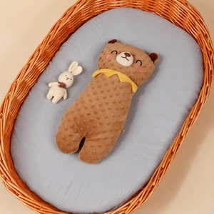 Detailed view of a brown bear-shaped minky fabric infant pillow in a wicker cradle