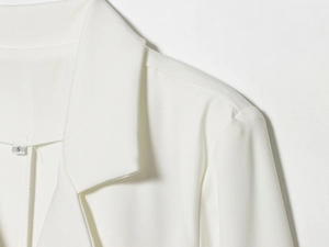 Detail view of a white tailored dress showing a notched lapel and high-quality fabric texture