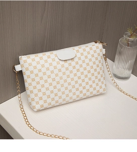 Close-up of white crossbody bag with golden clover pattern and metal chain strap