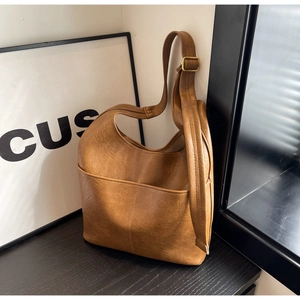 Detail einer braunen Hobo-Tasche aus Leder mit Vordertasche und goldener Hardware auf Holz