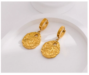 Detailed view of golden stainless steel earrings with irregular texture on a white stand
