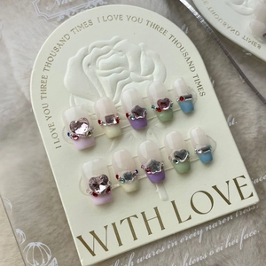 Detailed macro view of pastel press-on nails with heart rhinestones on display card