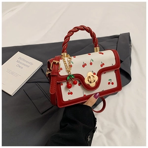 Detail of white cherry print handbag featuring a red twisted handle and floral gold clasp