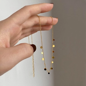 Detail of a gold choker necklace with small round charms held by a hand