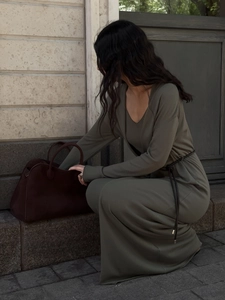 Close-up of olive green knitted maxi dress with a black belt and leather handbag